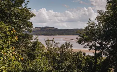 a view of a body of water between trees at Hampsfell Cottage, quaint and comfy by the Lake District in Grange Over Sands