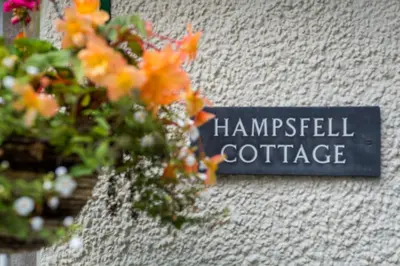 a sign on the side of a wall with flowers at Hampsfell Cottage, quaint and comfy by the Lake District in Grange Over Sands