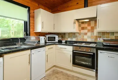 a kitchen with white cabinets and a sink and a microwave at Woodlands Hotel & Pine Lodges in Grange Over Sands