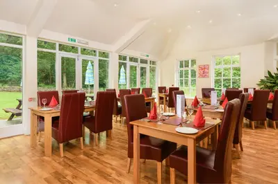 a dining room with wooden tables and chairs and windows at Woodlands Hotel & Pine Lodges in Grange Over Sands