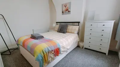 a bedroom with a bed with a rainbow blanket and a dresser at Bright, Comfortable Home, Convenient for City Centre in Liverpool