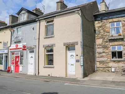 an old brick building with a red door on a street at Molly's Cottage in Grange Over Sands