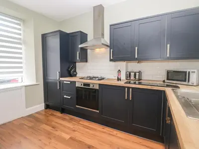 a kitchen with black cabinets and wooden floors at Molly's Cottage in Grange Over Sands