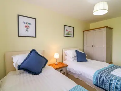a bedroom with two beds and a table with a lamp at Molly's Cottage in Grange Over Sands