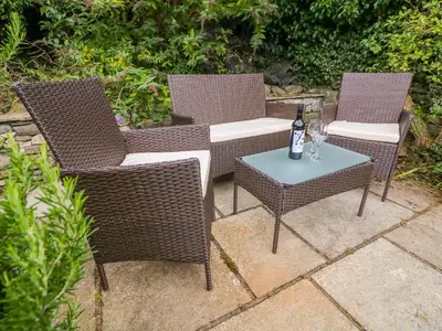 three wicker chairs and a table with a bottle of wine at Molly's Cottage in Grange Over Sands