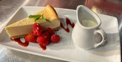 a white plate with a piece of cheesecake and strawberries at Raffles Hotel in Blackpool