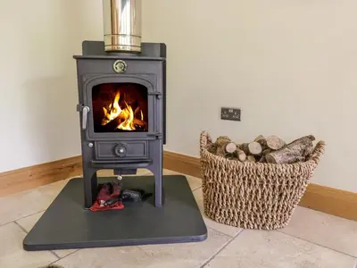 a wood stove in a room with a basket of logs at Neddy Cut in Ulverston