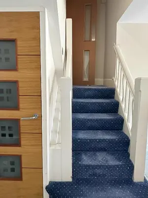 a staircase with blue carpeting and a wooden door at Granada Apartments Queens Mansions in Blackpool