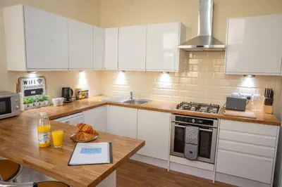 a kitchen with white cabinets and a wooden table at Sapphire House By Sasco in Blackpool