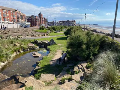 a park with a bench next to a river and the beach at The Mayfield Hotel in Blackpool