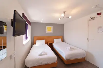 two beds in a small room with a tv at The Royal Alexandra Hotel by Compass Hospitality in Blackpool
