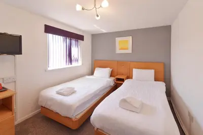 two beds in a small room with a tv at The Royal Alexandra Hotel by Compass Hospitality in Blackpool