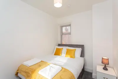 a white bedroom with a bed with yellow pillows at Cherry Property - Hornby Road in Blackpool