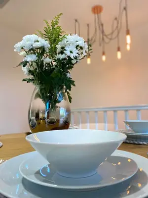 a white bowl on a table with a vase with flowers at Womack Lodge in Saint Helens