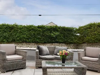 a patio with wicker chairs and a table with a vase of flowers at The Bothy in Beetham
