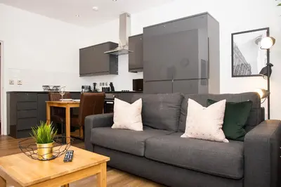 a living room with a gray couch and a kitchen at SGT Peppers Mathew Street Apartments By Happy Days in Liverpool