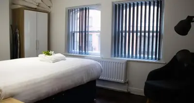 a bedroom with a bed and a chair and two windows at 27 Stanley Street Aparthotel by UStay in Liverpool