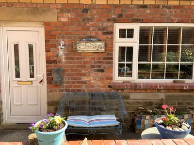 a chair sitting outside of a brick building with two potted plants at Beach Cottage in Lytham St Annes