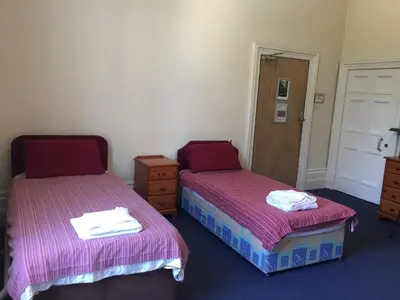 two beds in a room with purple sheets and a door at FSC Castle Head Hostel in Grange Over Sands