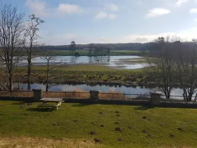 a bench sitting in the grass next to a river at FSC Castle Head Hostel in Grange Over Sands
