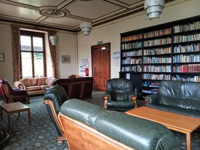 a living room with leather furniture and bookshelves at FSC Castle Head Hostel in Grange Over Sands