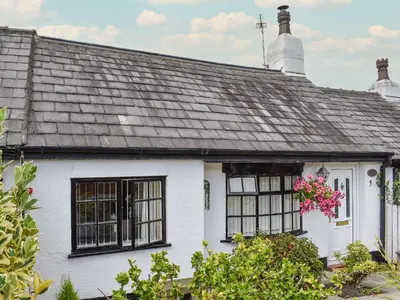 a white house with black windows and pink flowers at Sunnyside Cottage in Crossens
