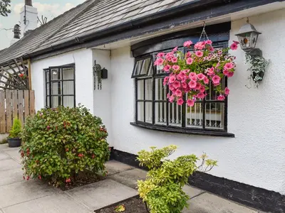 a white house with a window with pink flowers at Sunnyside Cottage in Crossens