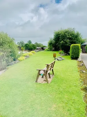 a wooden bench sitting on the grass in a park at Keer Side Lodge, Luxury lodge with private hot tub at Pine Lake Resort in Carnforth
