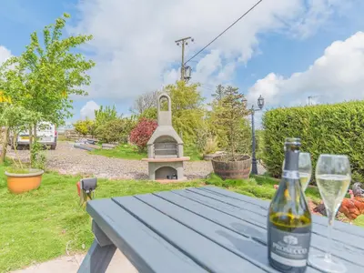 a bottle of wine sitting on a picnic table with two glasses at The Lodge in Dalton in Furness
