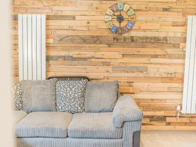 a couch in front of a wooden wall with a clock at The Lodge in Dalton in Furness