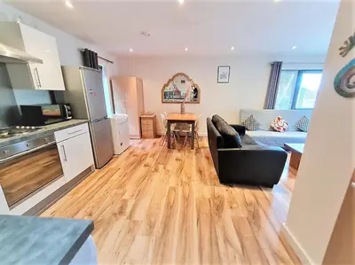 a living room with a black couch and a kitchen at Two-bedroom ground-floor apartment Self check-in in Liverpool