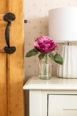 a pink rose in a vase on a table with a lamp at Maggie Puddle Cottage in Cartmel