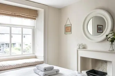 a white bedroom with a mirror and a fireplace at Maggie Puddle Cottage in Cartmel