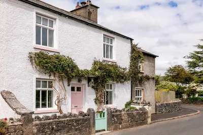 a white house with a pink door on a street at Maggie Puddle Cottage in Cartmel