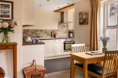a kitchen with white cabinets and a table and chairs at Maggie Puddle Cottage in Cartmel