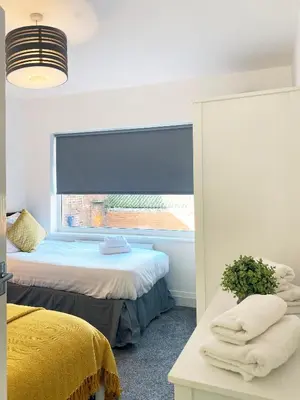 a bedroom with two beds and a window with a blue blind at The Baltic Townhouses by Serviced Living Liverpool in Liverpool