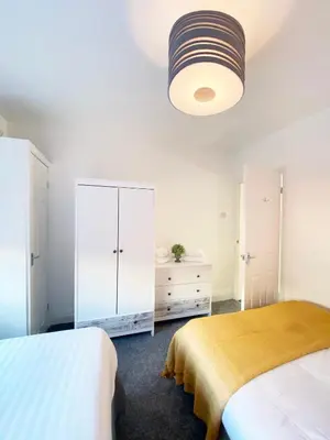 a white bedroom with two beds and a white cabinet at The Baltic Townhouses by Serviced Living Liverpool in Liverpool