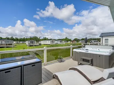 a patio with a hot tub and chairs on a deck at Links Lodge in Grange Over Sands