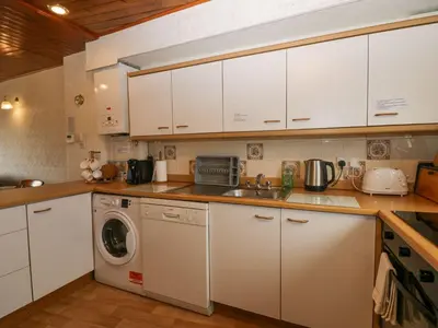 a kitchen with white cabinets and a washing machine at Lazey Cottage in Millom
