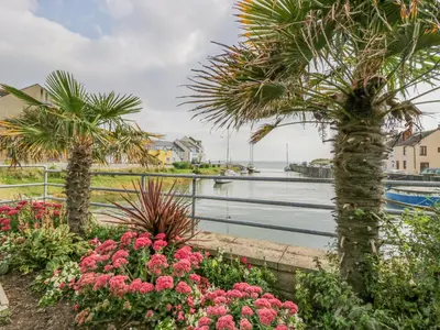 a garden with palm trees and flowers next to a body of water at Lazey Cottage in Millom