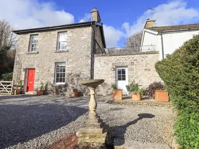 a stone house with a bird bath in front of it at Westmorland Cottage in Grange Over Sands