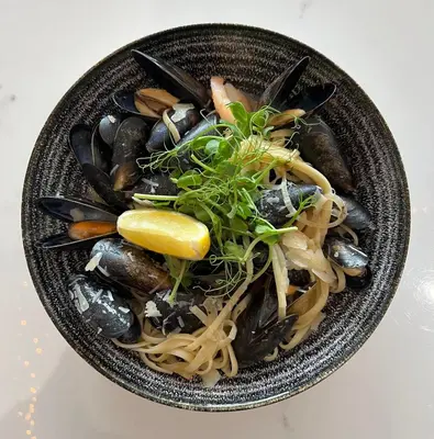 a bowl of noodles with mussels and a lemon at The Pheasant Inn in Grange Over Sands