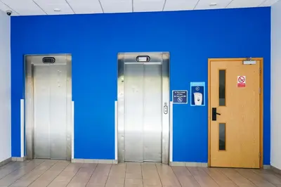three elevators in a building with a blue wall at GO2 Lancaster Centre Hotel by OYO in Lancaster