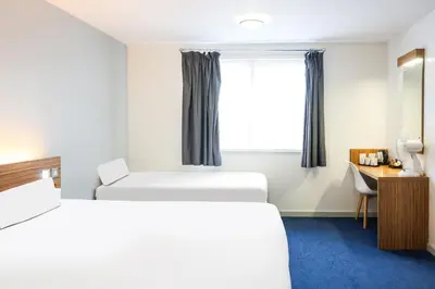 a bedroom with two beds and a desk and a window at GO2 Lancaster Centre Hotel by OYO in Lancaster