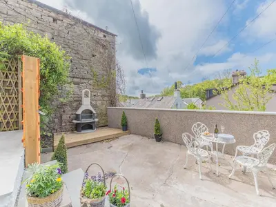 a patio with a table and chairs and a brick wall at Beeswax Cottage in Dalton in Furness