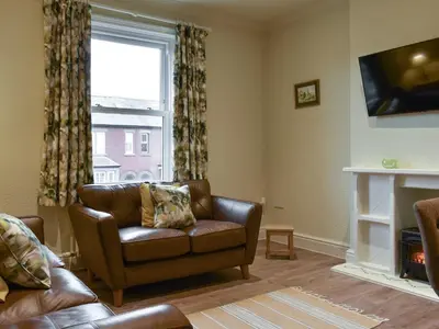 a living room with a leather couch and a window at Beachcomber Corner in Lytham St Annes