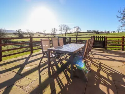 a wooden table and two chairs in front of a fence at Hill Brook Barn in Clitheroe