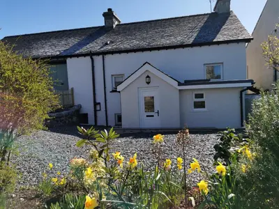 a white house with yellow flowers in front of it at Hillside Farm Cottage in Grange Over Sands