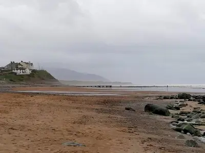 a beach with rocks and a house in the distance at Quirky bohemian Lake District miners cottage- 6 bd in Millom