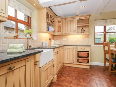 a kitchen with wooden cabinets and a tile floor at Laithe Cottage in Ulverston